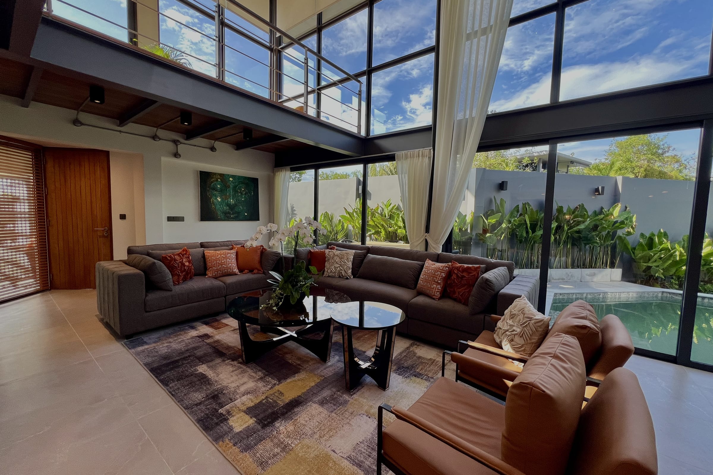 Интерьер индивидуальной виллы 4+ спальни RIVERHOUSE Phuket: двухсветная гостиная с панорамными окнами, просторной зоной отдыха и видом на частный бассейн и тропический сад.