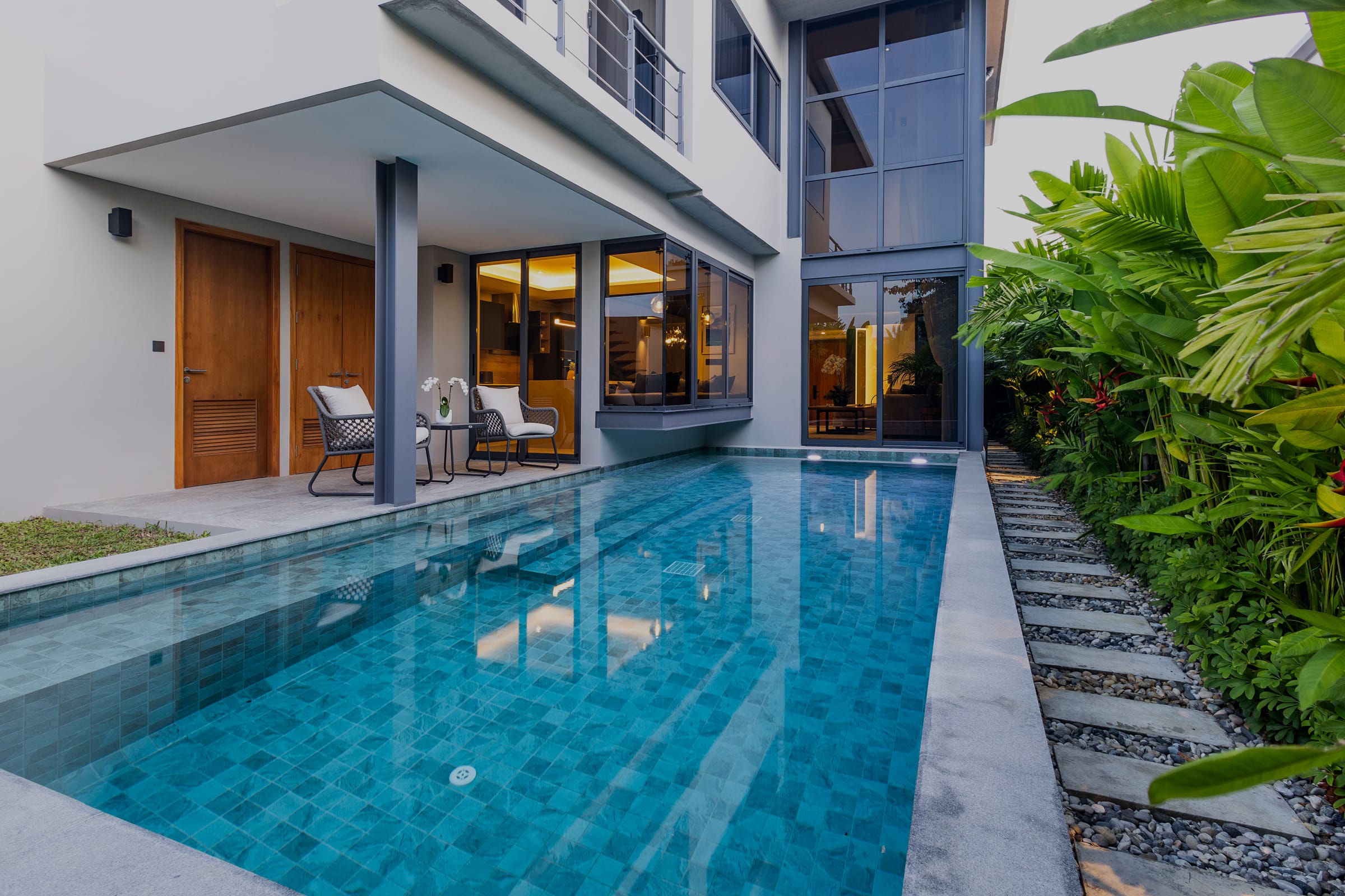 Современная вилла RIVERHOUSE Phuket с панорамными окнами в стиле лофт, тропическим садом и частным бассейном вдоль фасада.