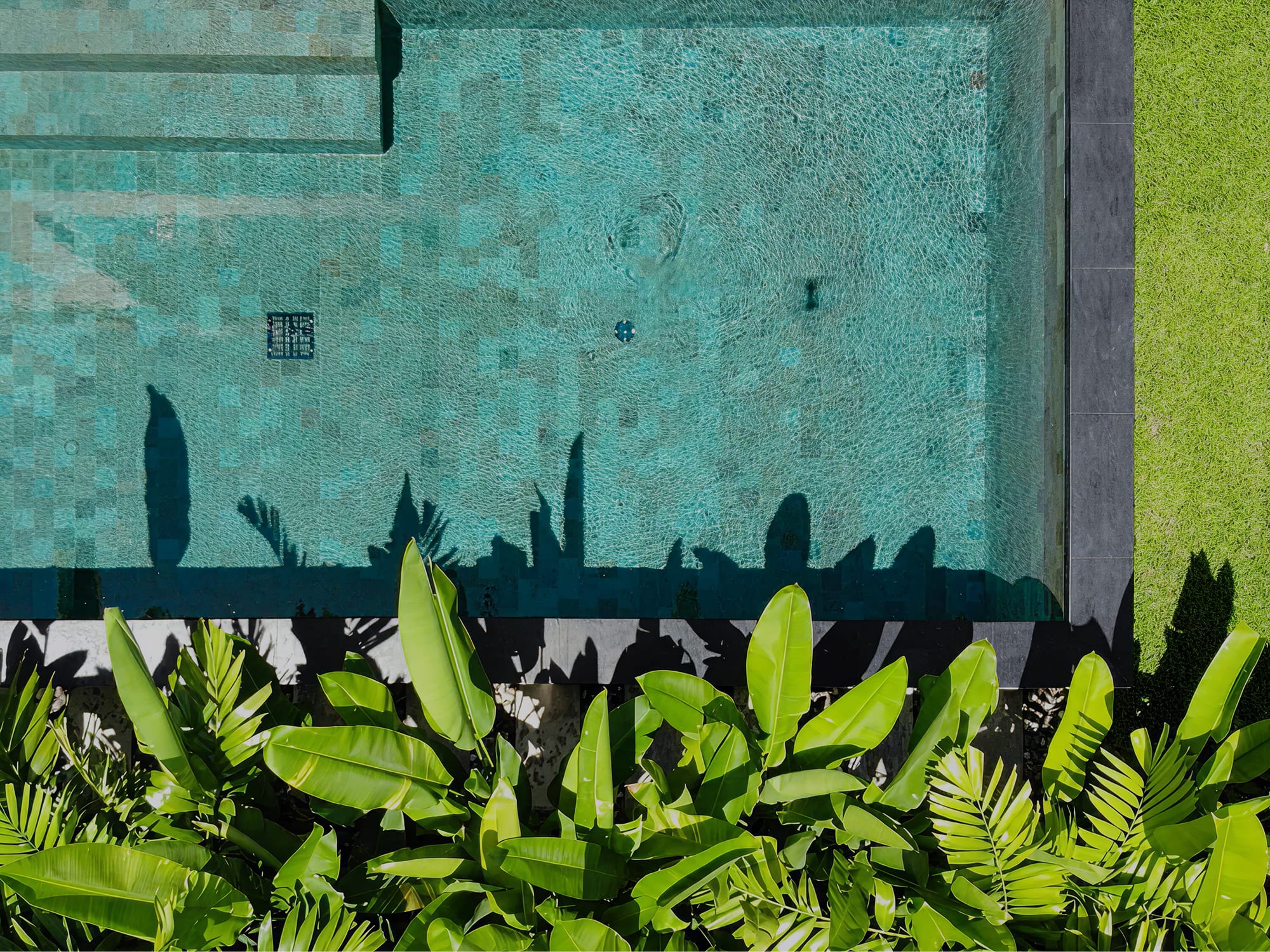 Вид сверху на частный бассейн виллы RIVERHOUSE Phuket с мозаичной плиткой и тропической зеленью вдоль борта.