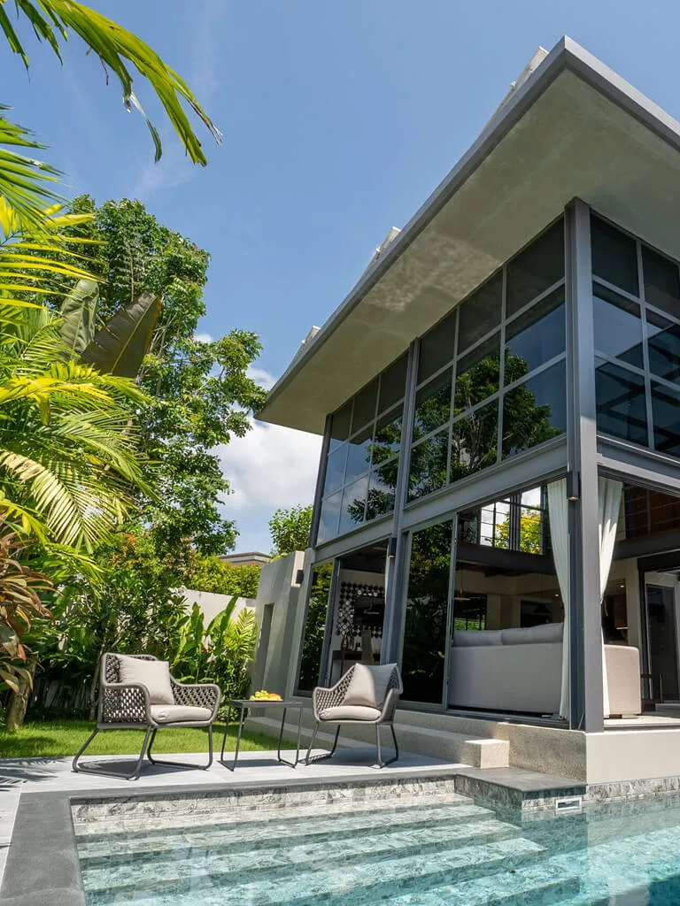 Вилла RIVERHOUSE Phuket с 3 спальнями: панорамные окна на два этажа, бассейн в центре планировки, терраса с зоной отдыха и зеленый сад вокруг.