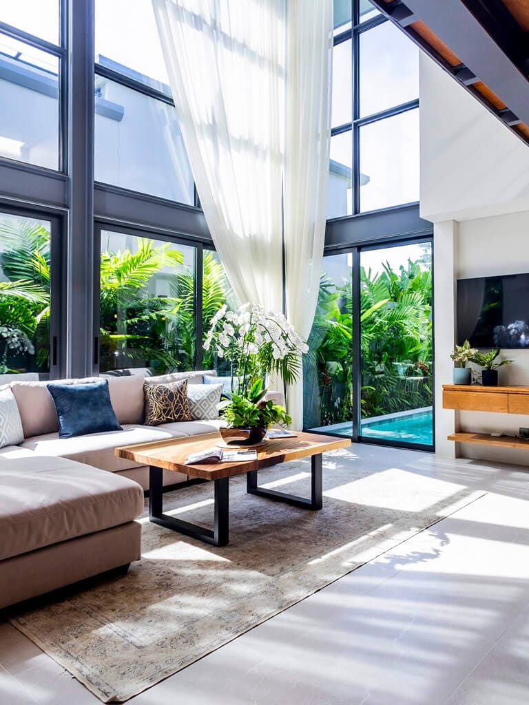 Светлая гостиная виллы с двумя спальнями в стиле лофт: панорамные окна 6 м, вид на частный бассейн и зелёный сад.